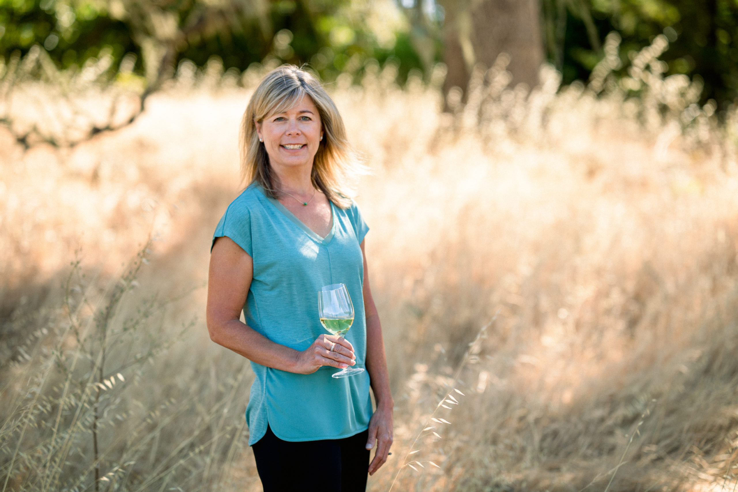 one woman standing in blue shirt with glass of white wine in hand