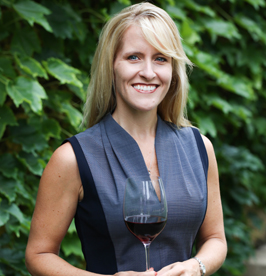 Lisa Mattson holding a glass of red wine in front of green ivy