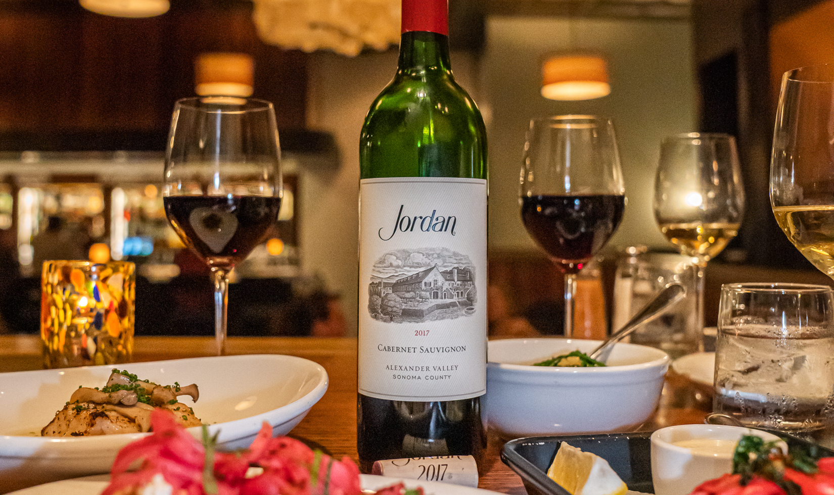 bottle of cabernet wine on restaurant table with wine glasses and food