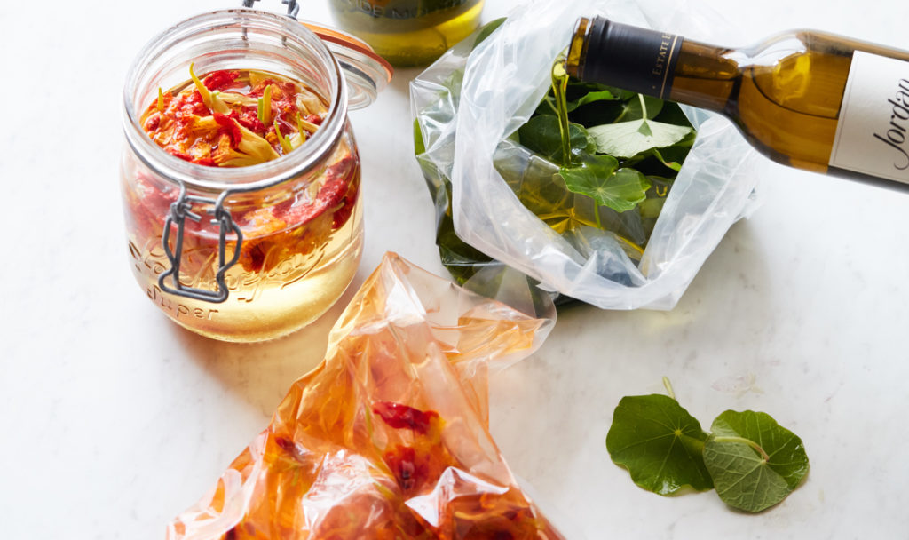 red and yellow flowers infused with verjus in clear mason jar with leaves and olive oil in a clear bag