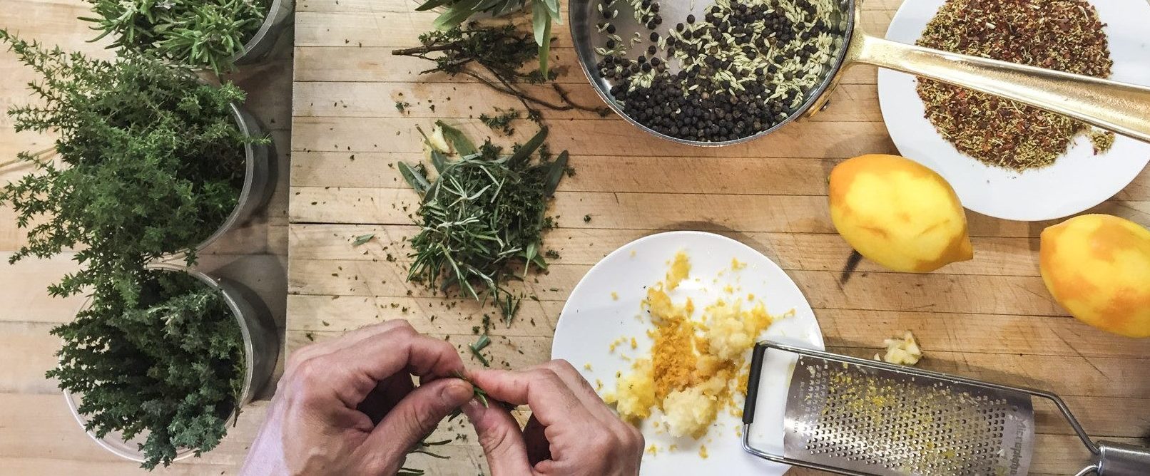hands pinching at herbs next to a plate with lemon zest and ingredients in a pot