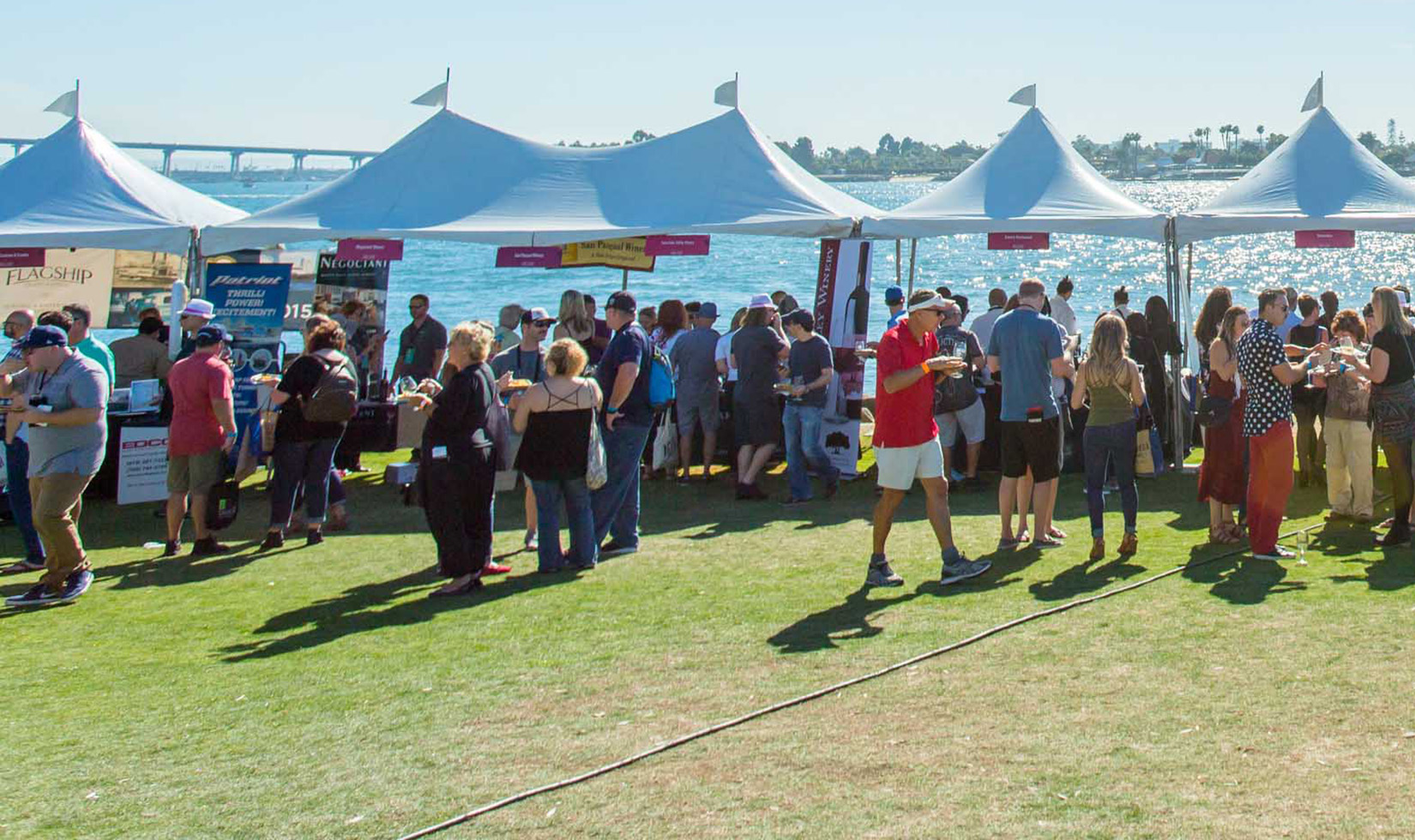 People eating and drinking in front of white tents with ocean in the background