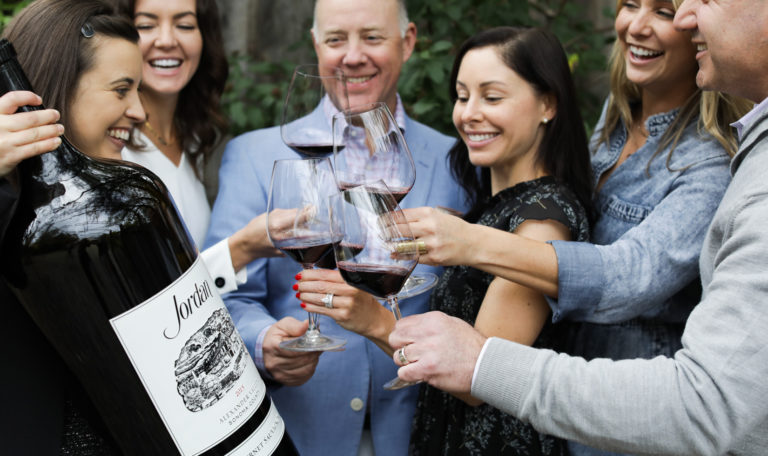 group of people toasting cabernet around a big bottle of wine