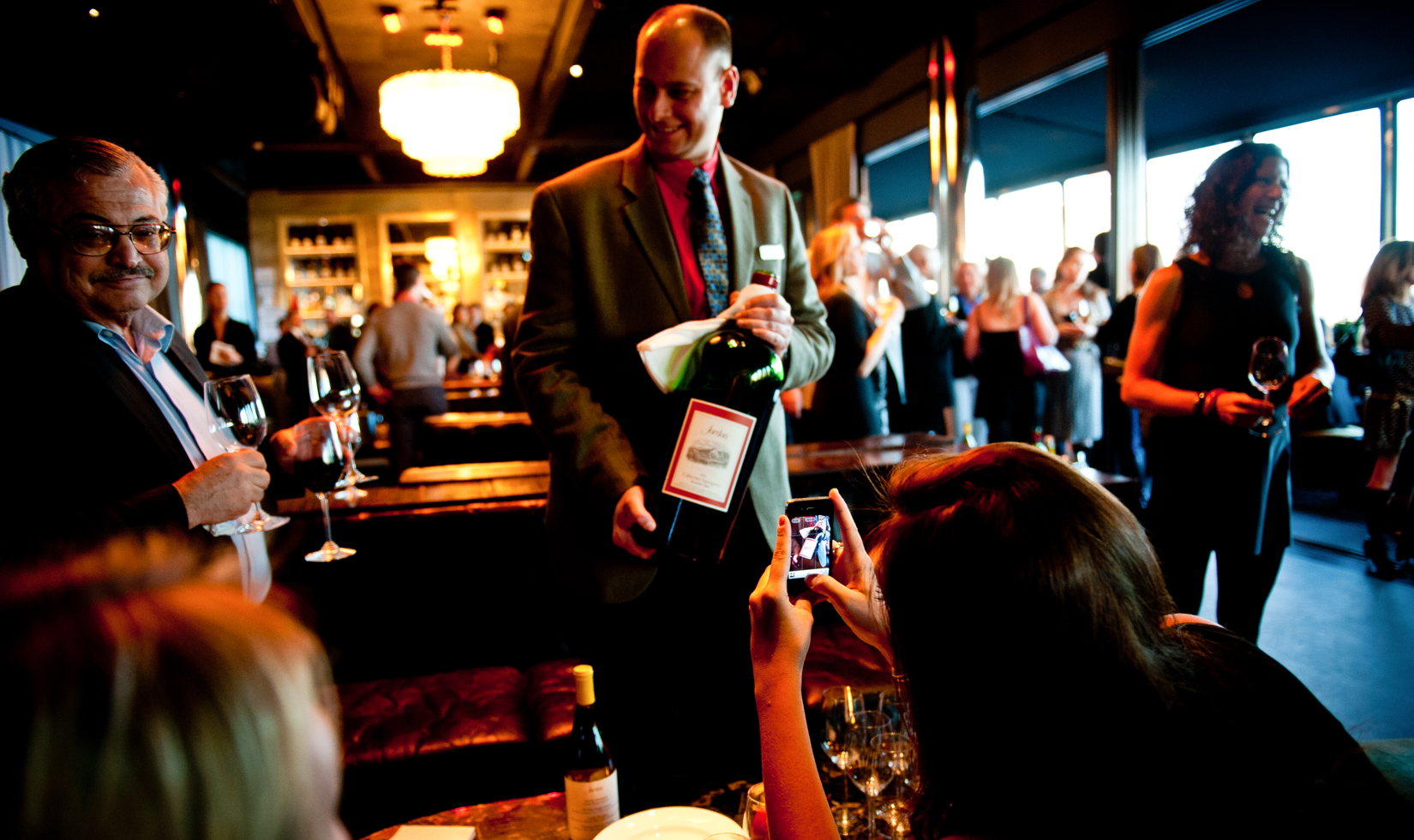 server holding large bottle of wine while someone takes a photo