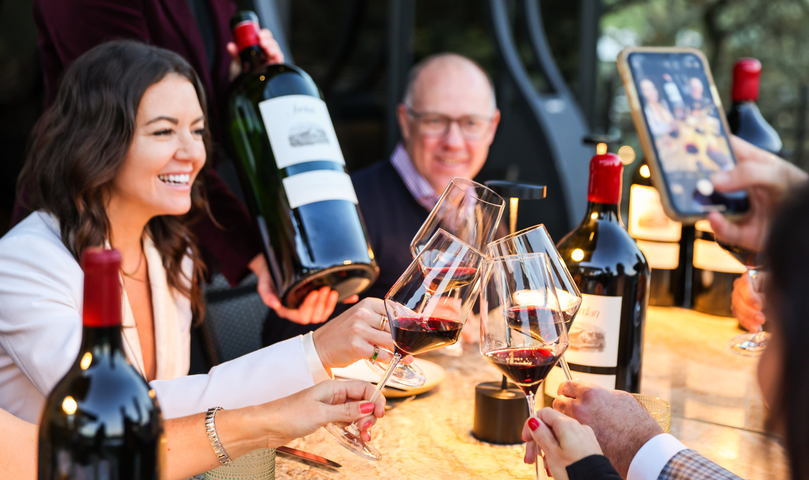 people toasting red wine glasses at dinner table with big wine bottle