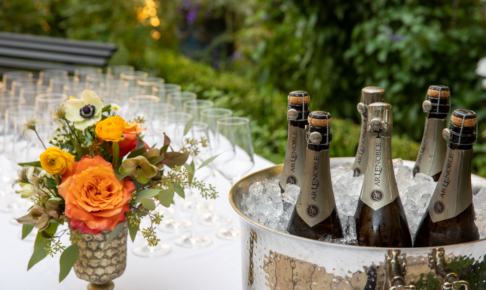 champagne in ice bucket with flowers and glasses on table