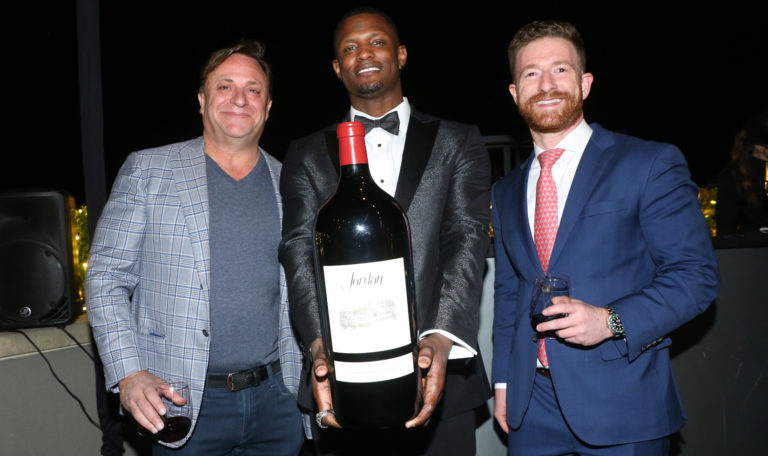 three men smiling and posing with big bottle of wine