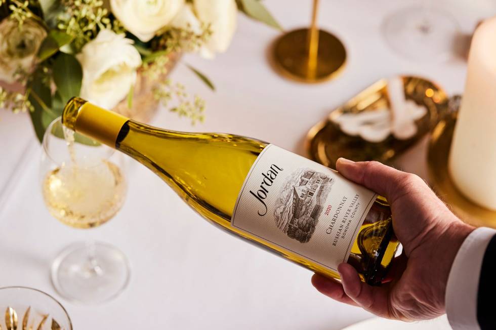 bottle of jordan chardonnay pouring into wine glass on formal dining table