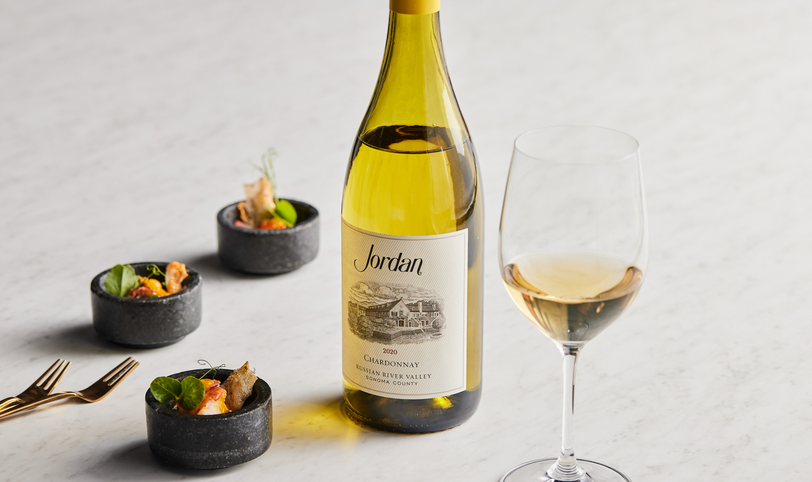 bottle of chardonnay on marble table with appetizers and glass of white wine