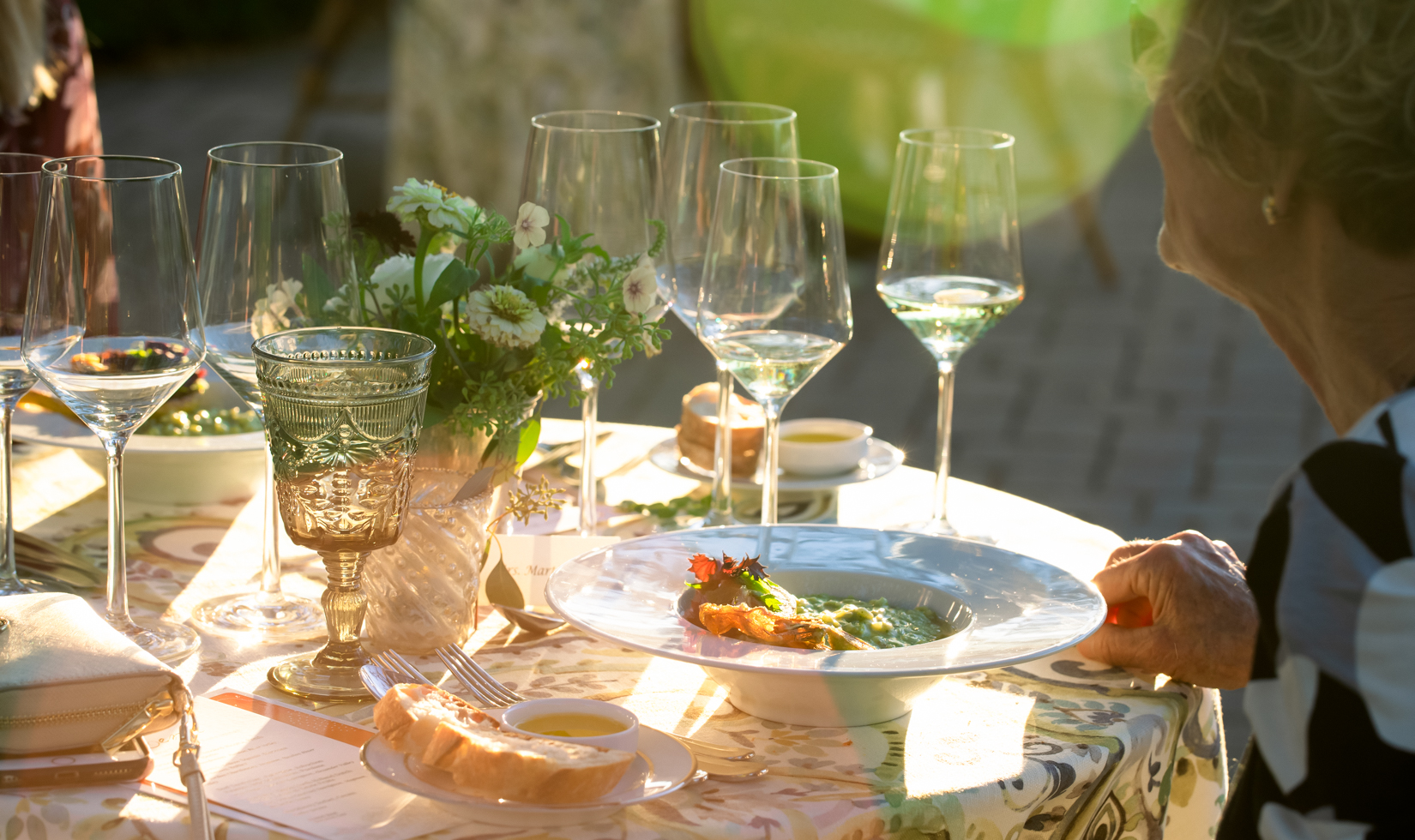 woman with plate of food and wine glasses at an outdoor dinner table