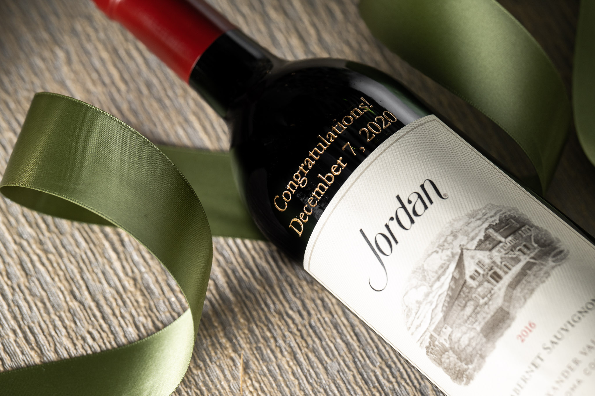 Etched cabernet bottle with custom message on table with decorative green ribbon