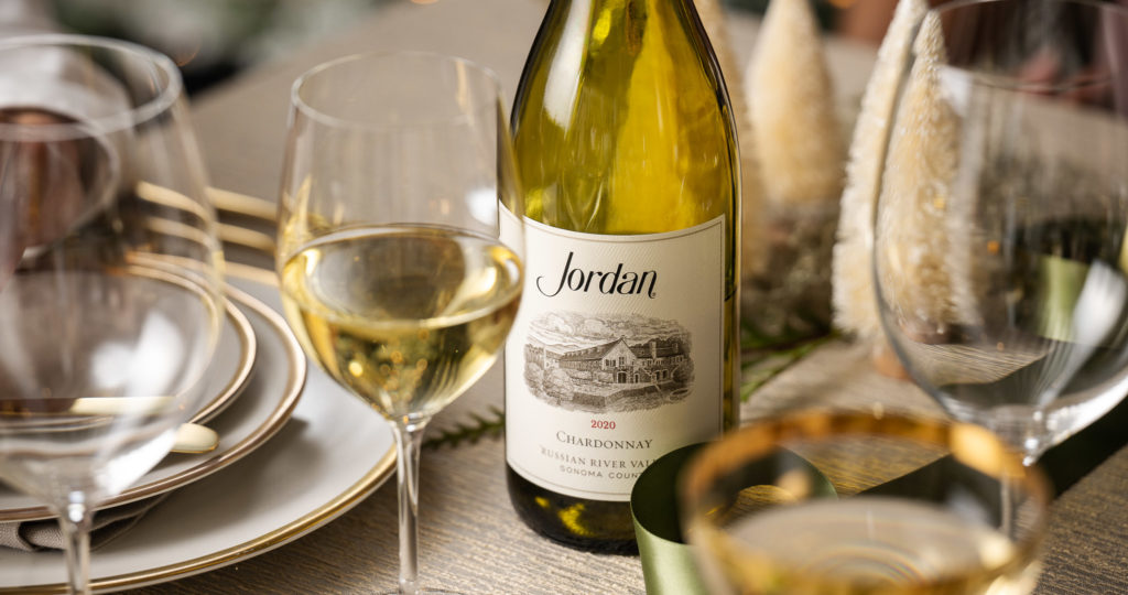 bottle of chardonnay on table set for Christmas dinner with festive pine cones on table