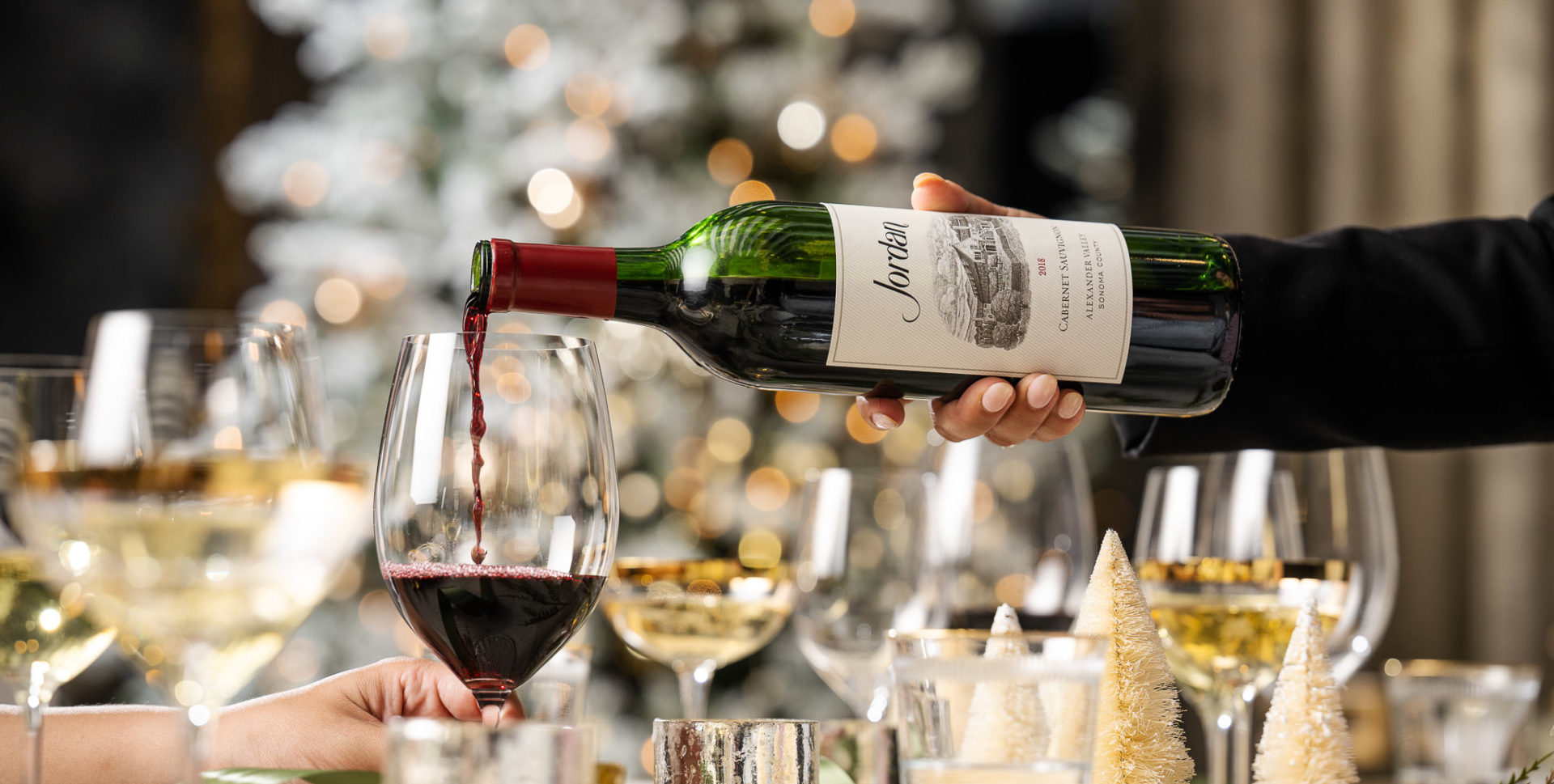 cabernet bottle pouring into wine glass with christmas tree in background