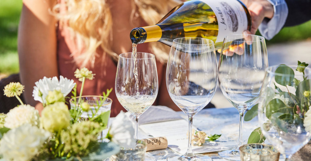 bottle of Jordan Chardonnay pouring for woman sitting at outdoor dinner table