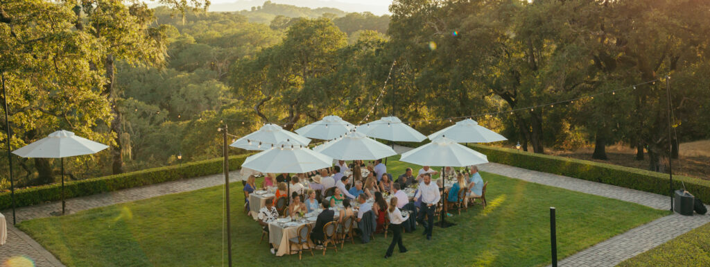group dining on winery terrace at long tables under white umbrellas