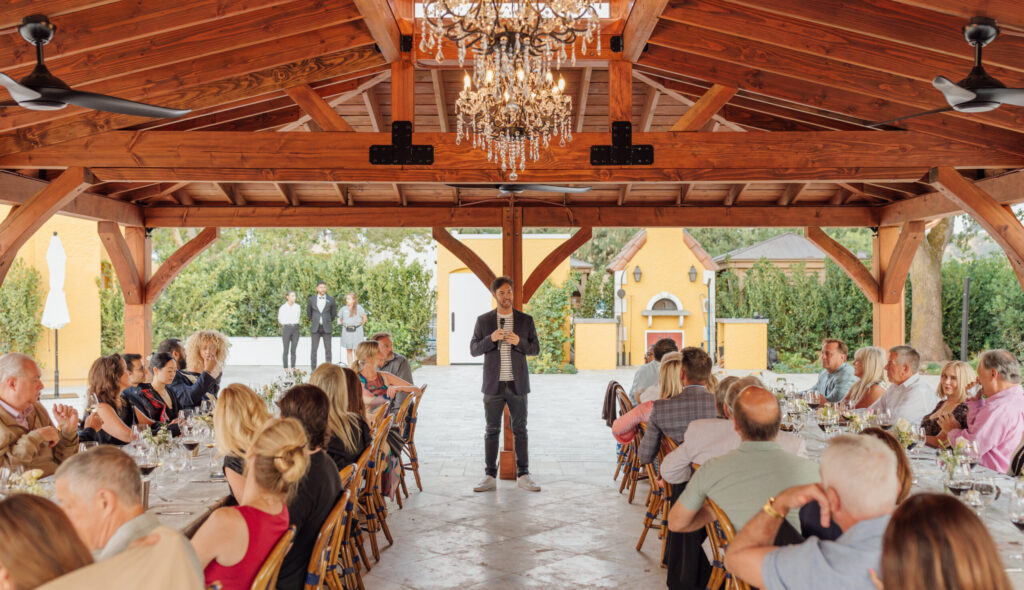 man speaking to group of dinner attendees outdoors