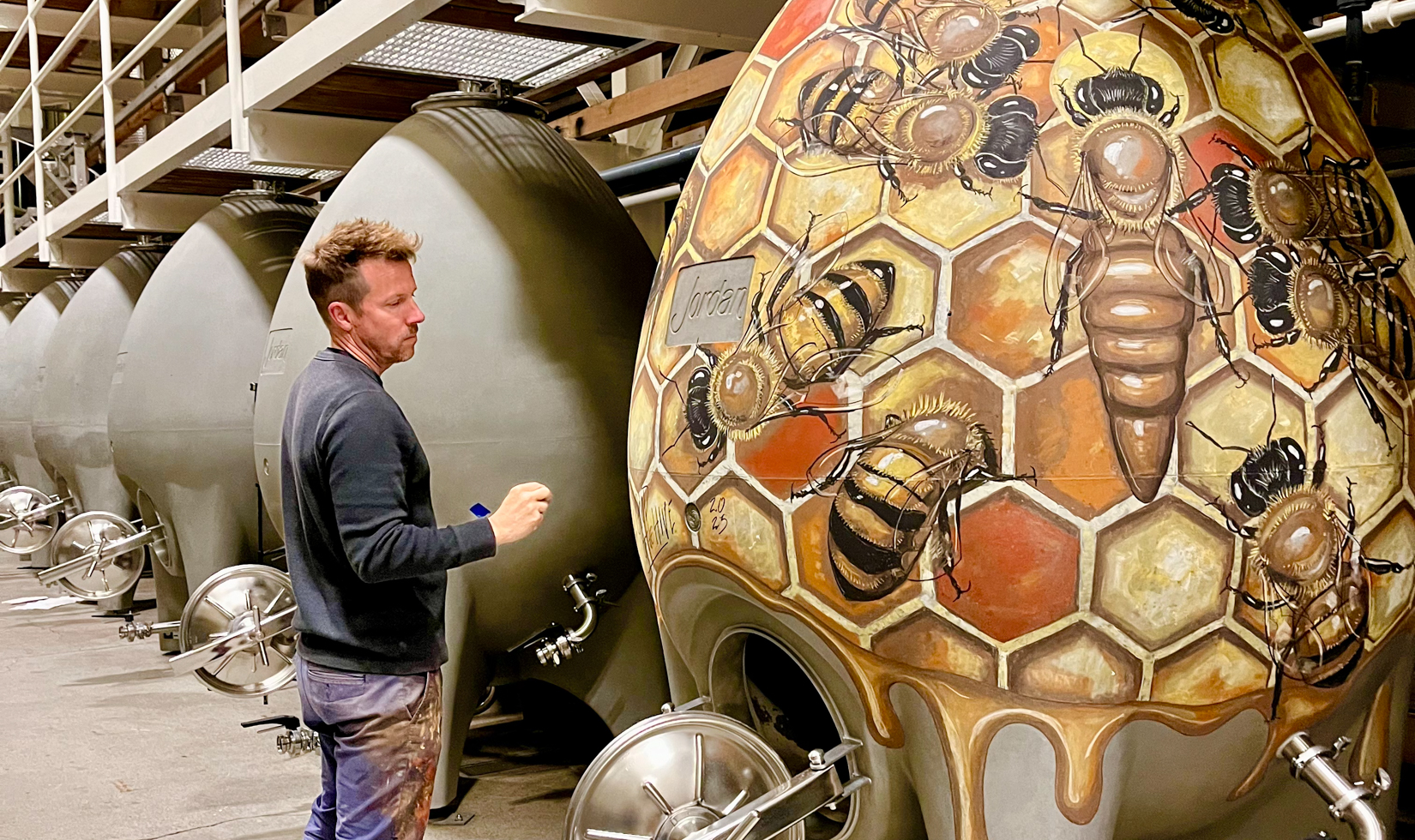 man standing next to honey bee art mural in winery barrel room