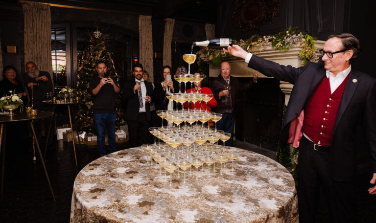 man pouring a bottle of champagne on the top of champagne glass tower