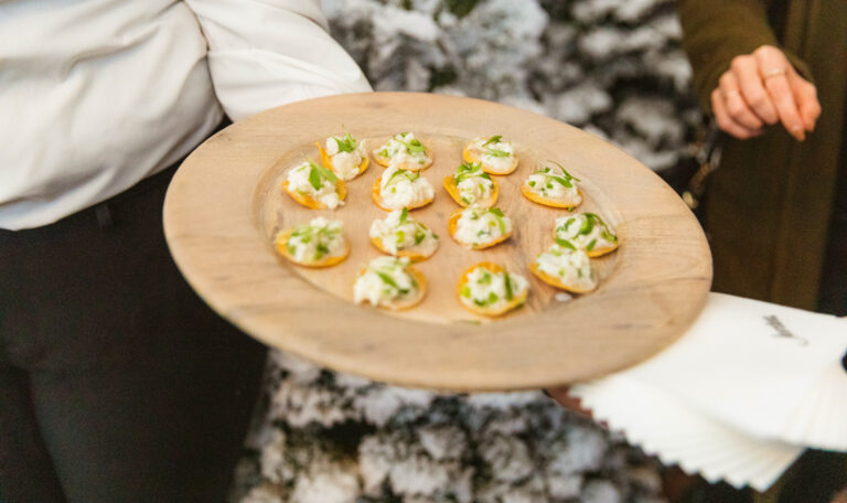 person holding tray of passed hors d'oeuvres by christmas tree