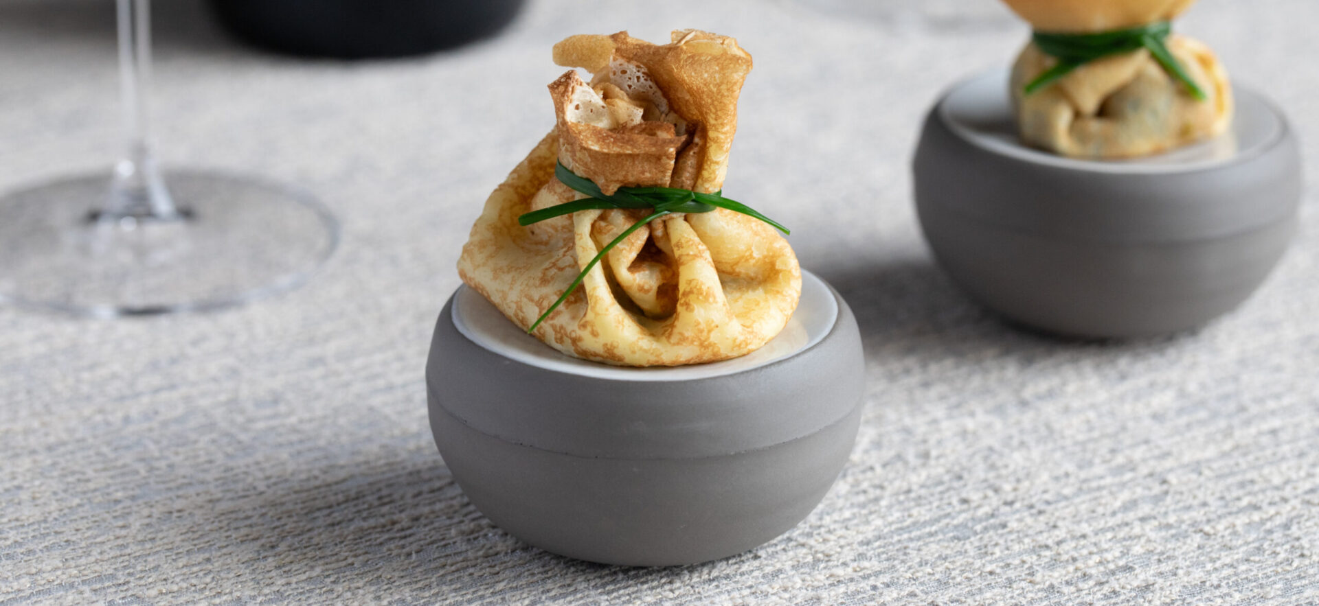 crepe bite folded with green chive filled with caviar. sitting on grey dish.