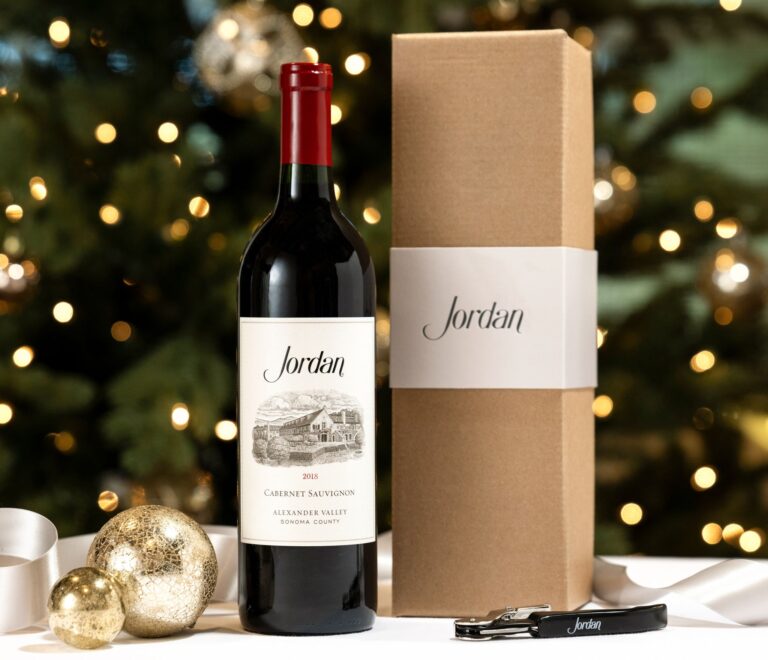 bottle of 2018 jordan cabernet sauvignon next to gift box with a black corkscrew with jordan logo on table decorated with christmas ornaments and silver ribbons