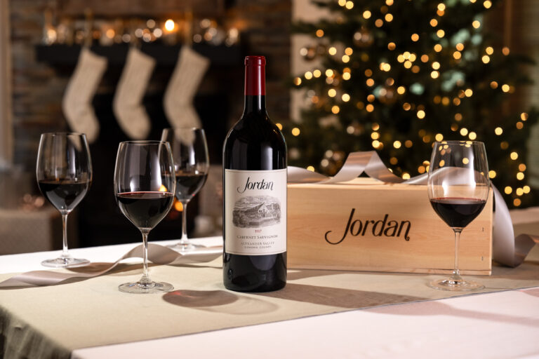 cabernet sauvignon bottle with wooden wine box and wine glasses on table with christmas tree and stockings in the background