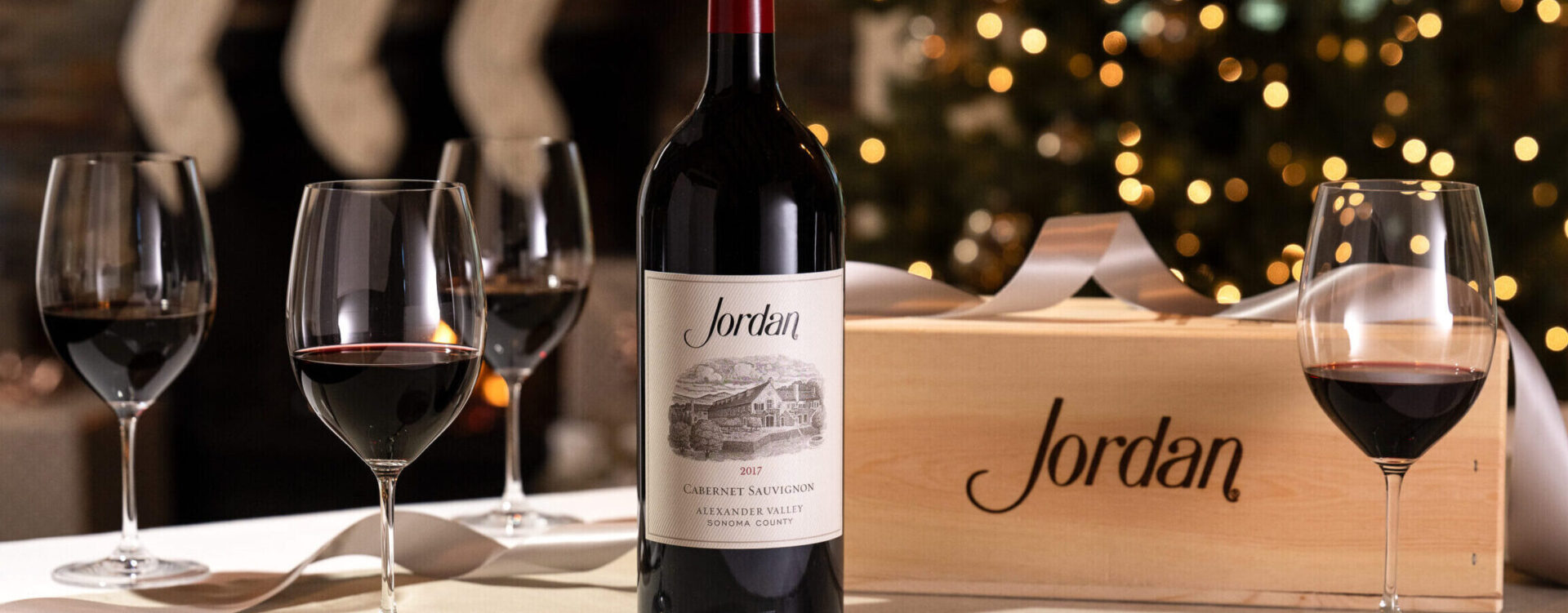 cabernet sauvignon bottle with wooden wine box and wine glasses on table with christmas tree and stockings in the background