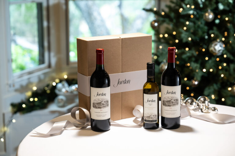 jordan cabernet and jordan estate extra virgin olive oil with gift box on table with silver ribbon and ornaments with christmas tree in background