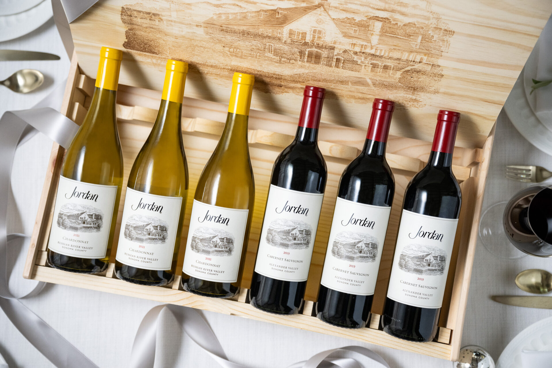 a wooden gift box with three bottles of jordan chardonnay and and three bottles of jordan cabernet framed by a silver festive ribbon