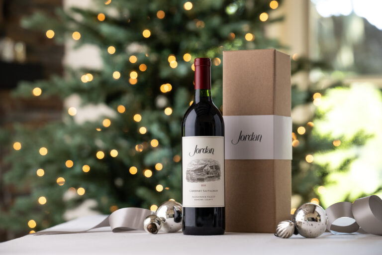 bottle of jordan cabernet sauvignon next to gift box on table silver christmas ornaments and ribbon