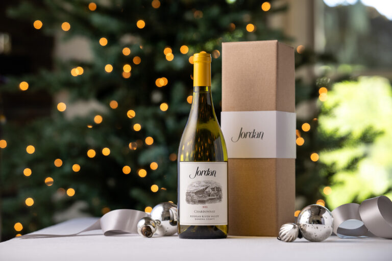 bottle of jordan chardonnay next to gift box on table silver christmas ornaments and ribbon