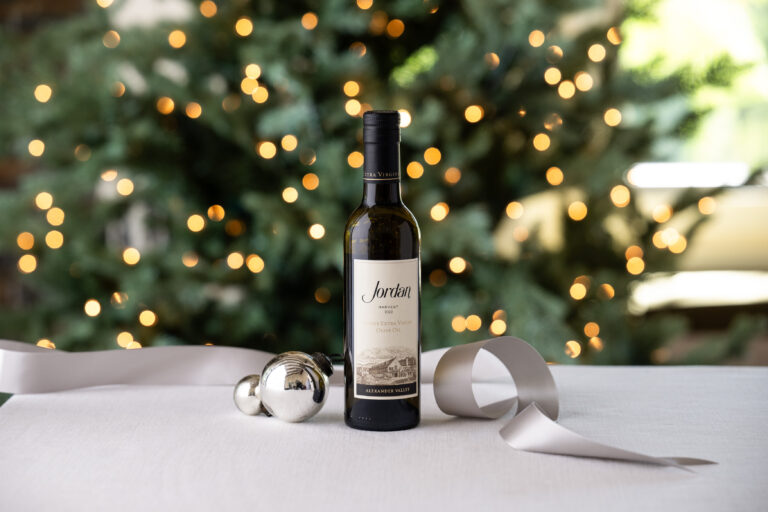 bottle of jordan estate extra virgin olive olive with silver ribbon and ornament with a christmas tree in background