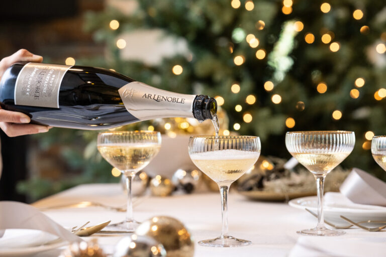 pouring jordan cuvee champagne into champagne coups on a table decorated for the holiday season with a christmas tree in the background