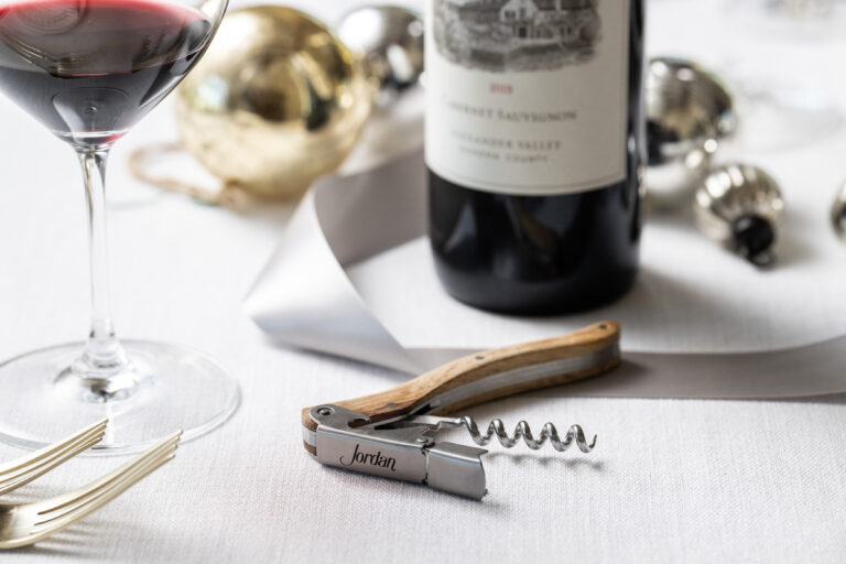 wooden corkscrew on white table cloth with silver ribbon and jordan cabernet bottle in background