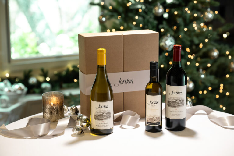jordan chardonnay, jordan cabernet sauvignon and jordan estate extra virgin olive oil on table with gift box and christmas decorations with a christmas tree in the background