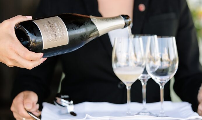 bottle of champagne pouring into wine glasses on service tray