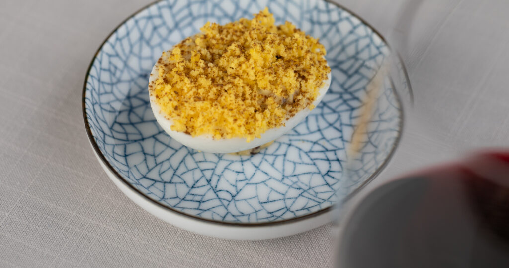 deviled egg on blue appetizer plate with a glass of cabernet wine