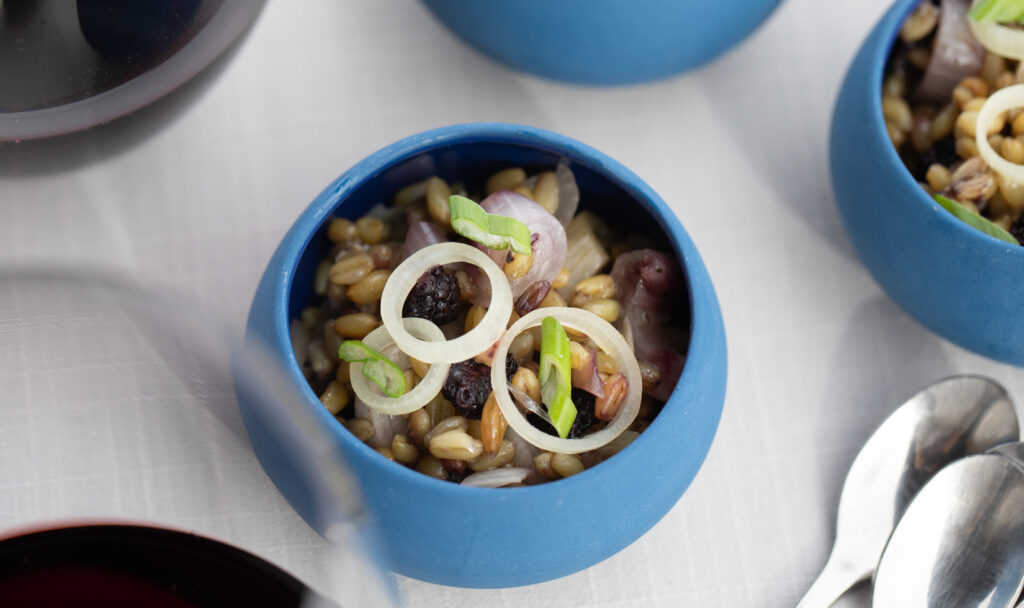 appetizer salad in a small blue bowl next to glass of red wine and spoons