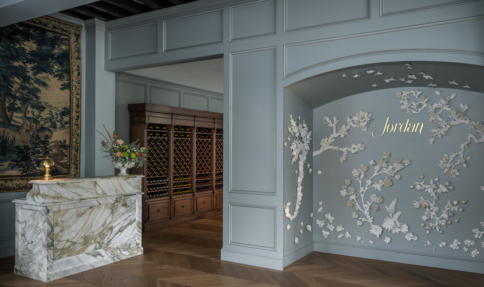 French-inspired lobby with robin's blue wall panels, a marble concierge desk with ornate tapestry and antique wine cellar wall in the background