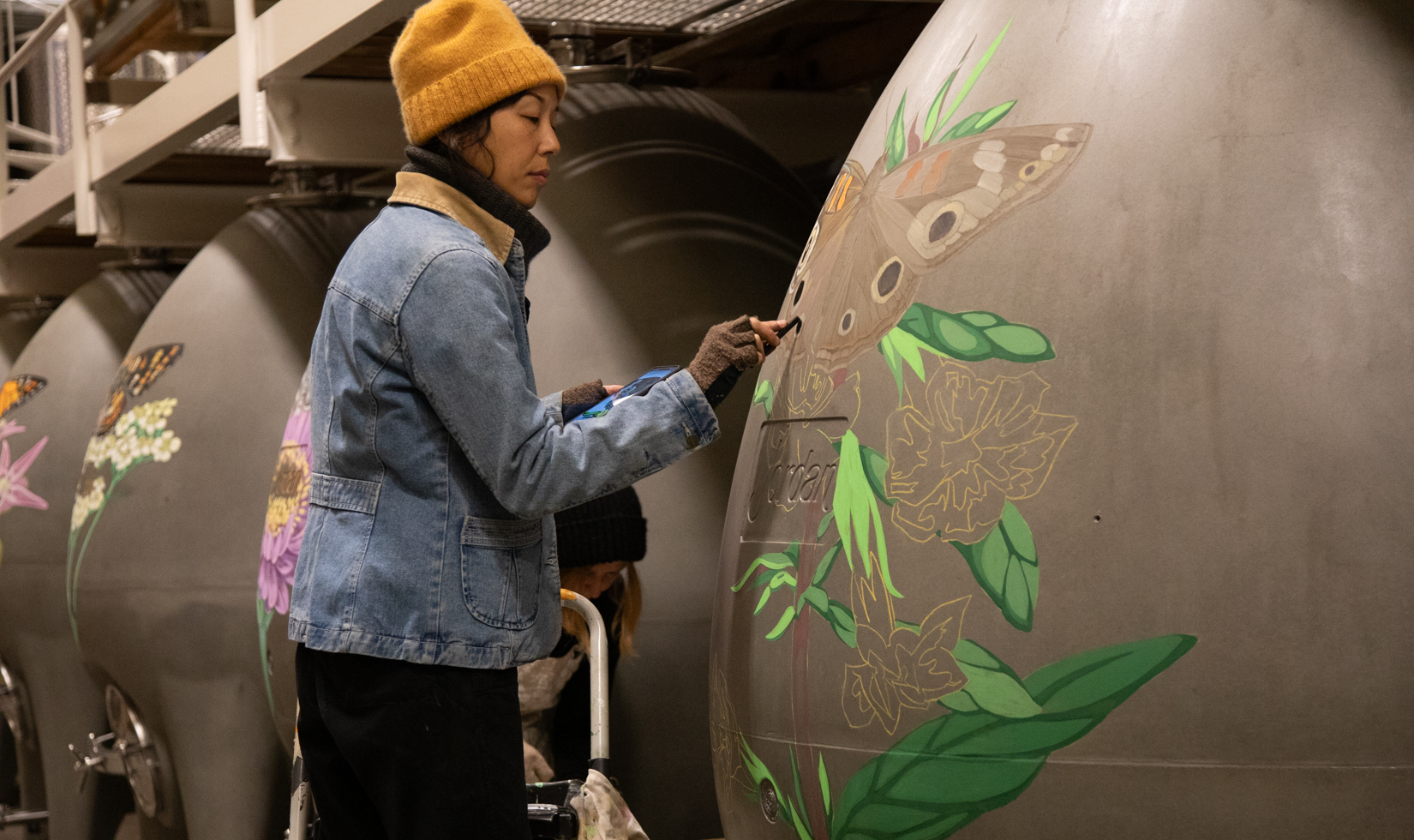 artist drawing a butterfly with pastel chalk on concrete egg wine fermenter