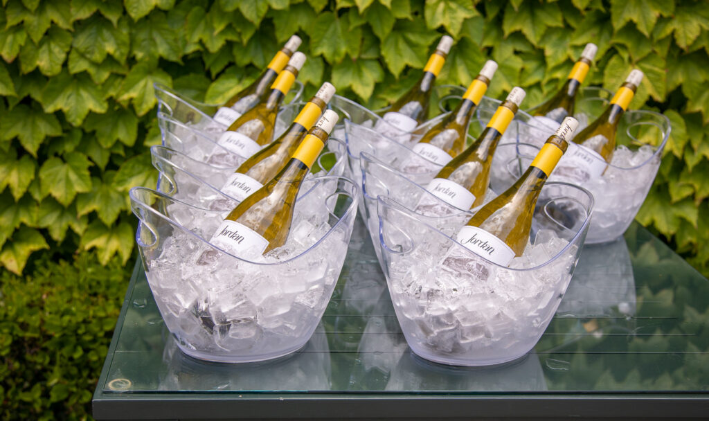 Ten bottles of Jordan Chardonnay in individual ice buckets on outdoor table