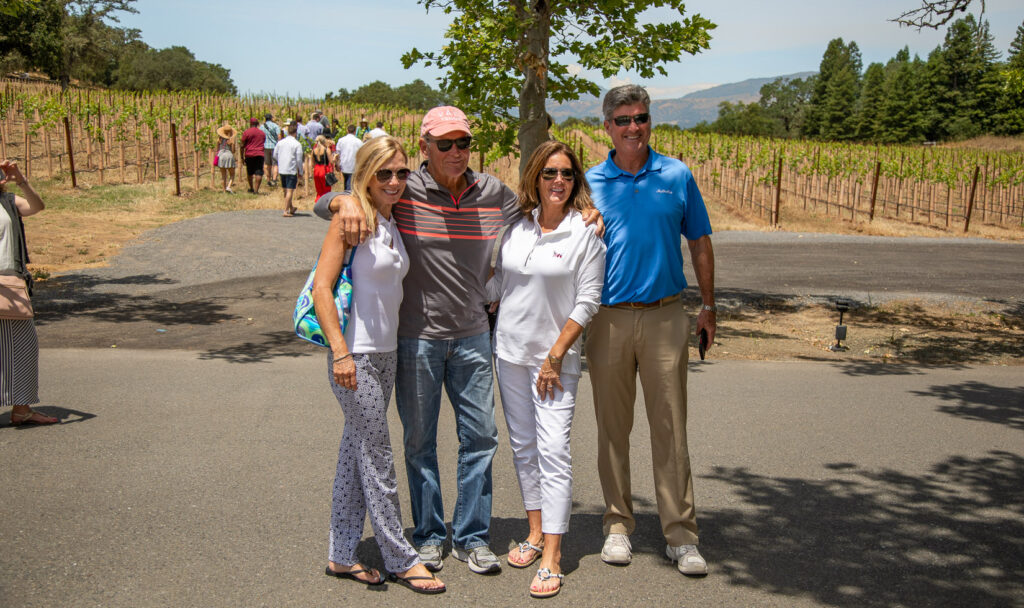 group of four guests posing in front of vineyard vines before the picnic