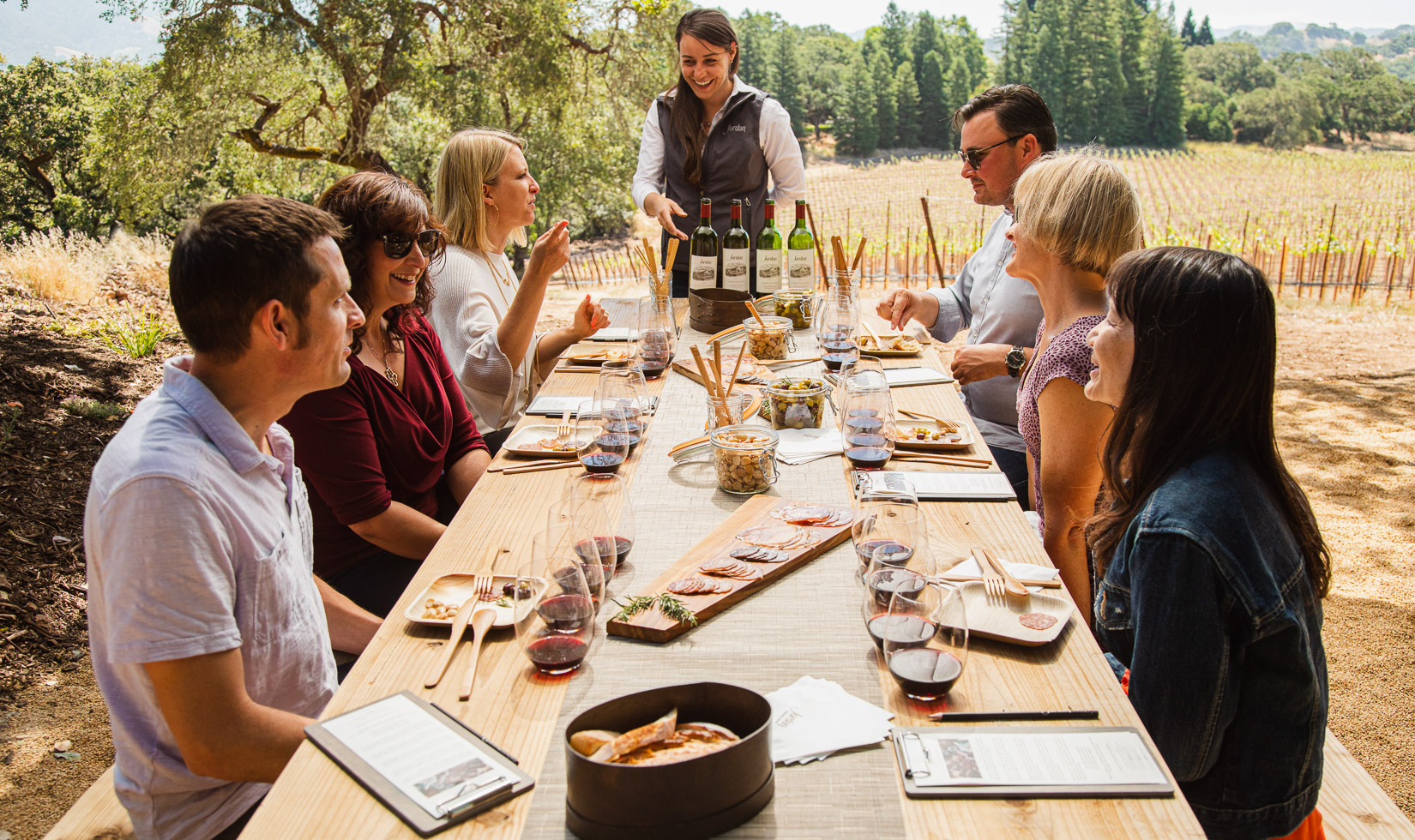 group at picnic table in vineyard with wine tasting and small bites on table