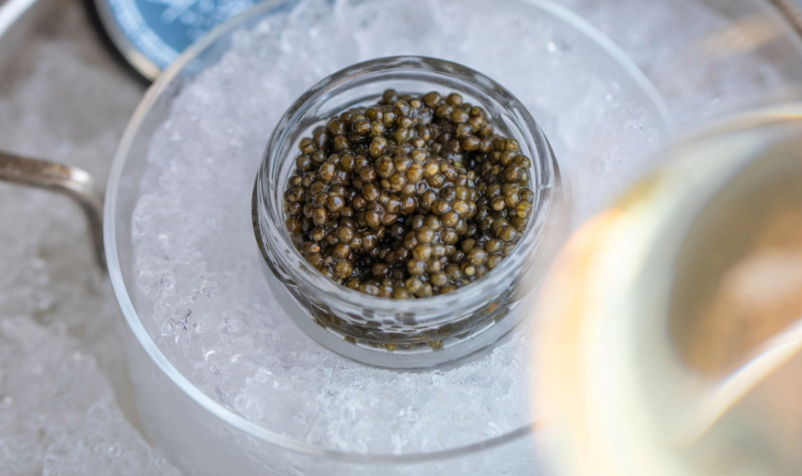 closeup image of caviar in glass jar resting on tray filled with ice