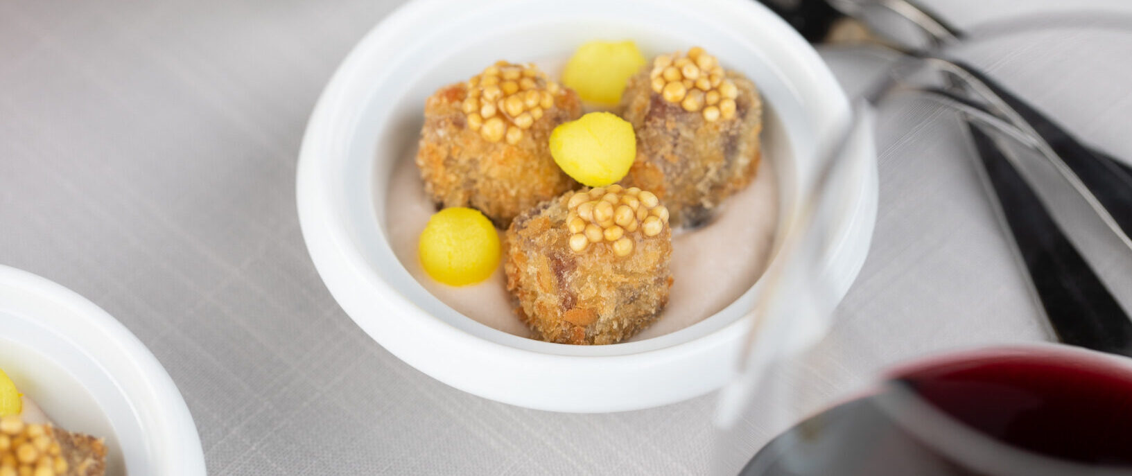 Crispy Short Ribs with Radish Soubise and Pickled Mustards Seeds & Daikon in small white bowls with glasses of red wine and forks on table