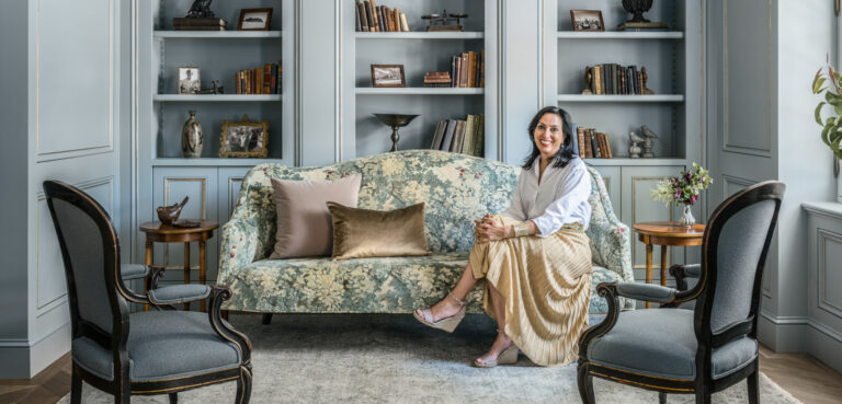 woman wearing white shirt and gold skirt sitting on sofa in a blue paneled library room