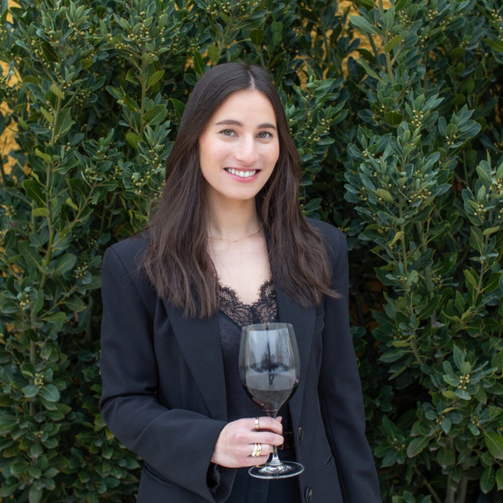 Anaelle Laplume standing in front of ivy-covered wall with a glass of red wine in hand