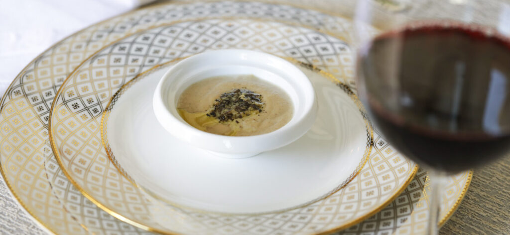 Porcini Mushroom Fondue on white and gold plate with glass of red wine