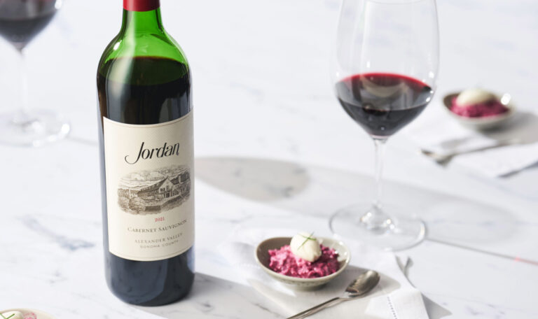 Bottle of Jordan Cabernet Sauvignon on white marble counter next to plated hors d'oeuvres and a wine glass