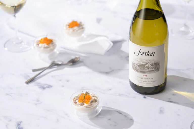Bottle of Jordan Chardonnay on white marble counter next to plated hors d'oeuvres and a wine glass